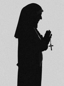 Nun in silhouette praying while holding a rosary.