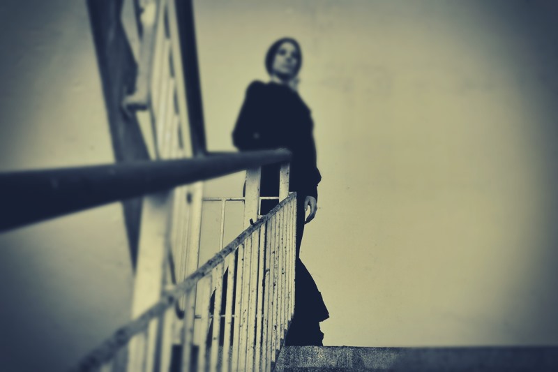 Ghostly woman in black dress standing at top of stone staircase